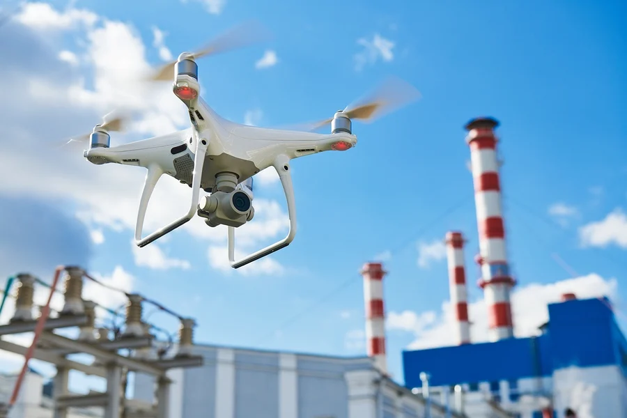 drone equipped with a camera flies over an industrial plant with red-and-white smoke stacks in the background